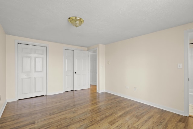unfurnished bedroom featuring a textured ceiling, baseboards, two closets, and wood finished floors
