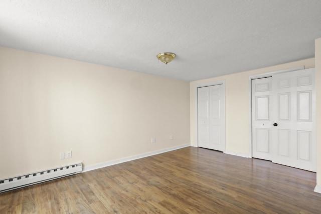 unfurnished bedroom with wood finished floors, baseboards, two closets, and baseboard heating