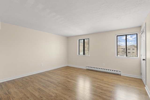 empty room with baseboards, baseboard heating, wood finished floors, and a wealth of natural light