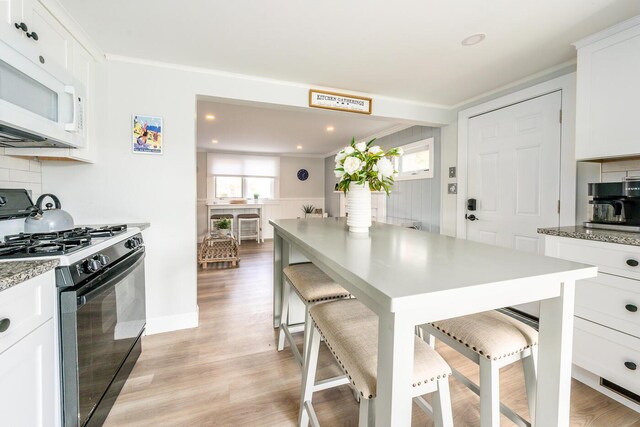 kitchen featuring gas stove, white cabinetry, light hardwood / wood-style floors, backsplash, and a breakfast bar