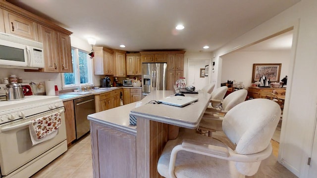 kitchen with appliances with stainless steel finishes, a kitchen island, a kitchen bar, sink, and light tile patterned flooring