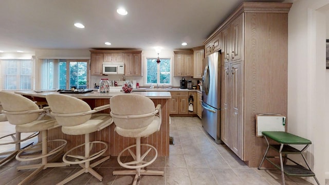 kitchen featuring decorative light fixtures, light brown cabinets, a kitchen bar, and stainless steel refrigerator