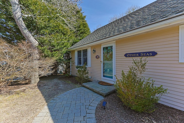 property entrance with a shingled roof and a patio area