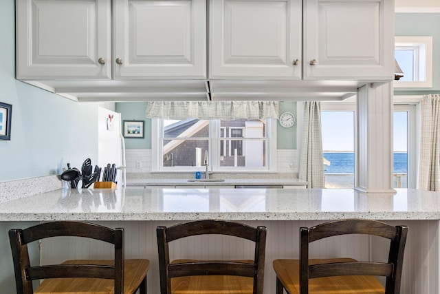 kitchen featuring sink, a breakfast bar area, white cabinets, light stone counters, and a water view