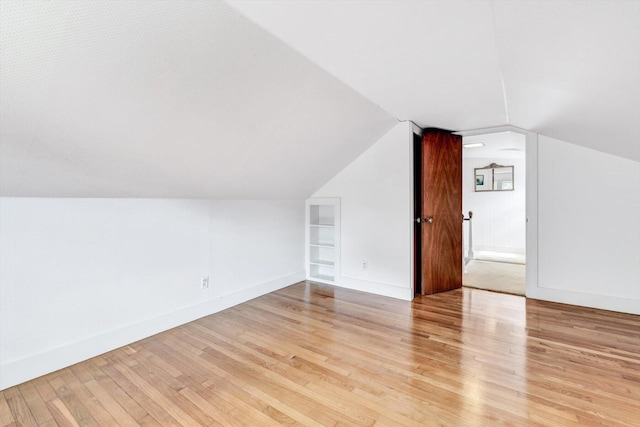 bonus room featuring light wood-type flooring, vaulted ceiling, and built in features