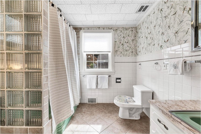 bathroom featuring vanity, toilet, tile walls, and tile patterned floors