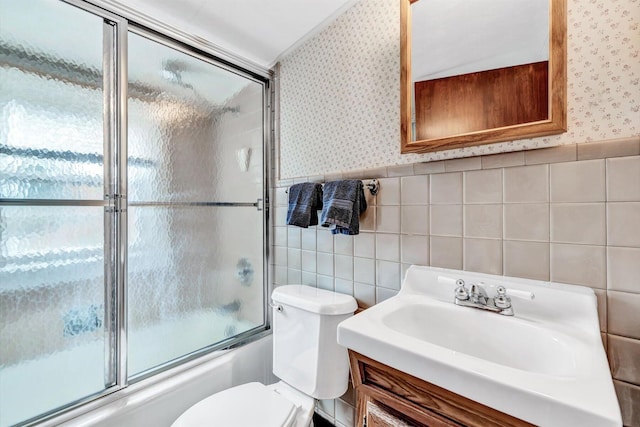 full bathroom featuring vanity, a healthy amount of sunlight, tile walls, toilet, and combined bath / shower with glass door