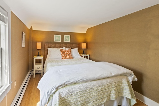 bedroom with a baseboard radiator, wood finished floors, and baseboards