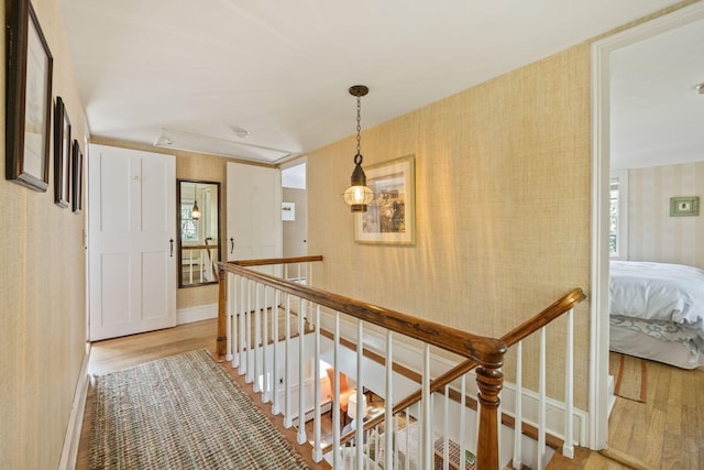 hall featuring wallpapered walls, an upstairs landing, light wood-style flooring, and baseboards