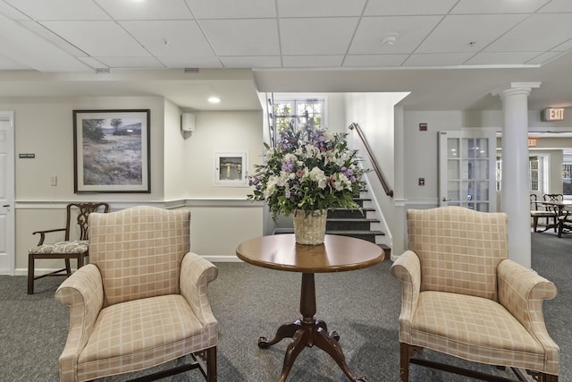 living area featuring carpet, ornate columns, and a drop ceiling