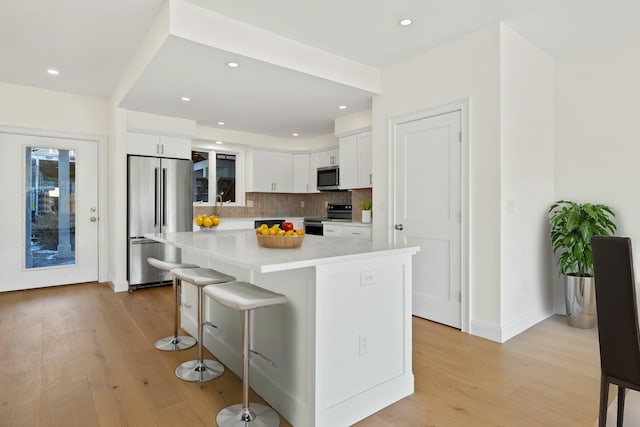 kitchen with a kitchen island, a breakfast bar, white cabinets, decorative backsplash, and stainless steel appliances