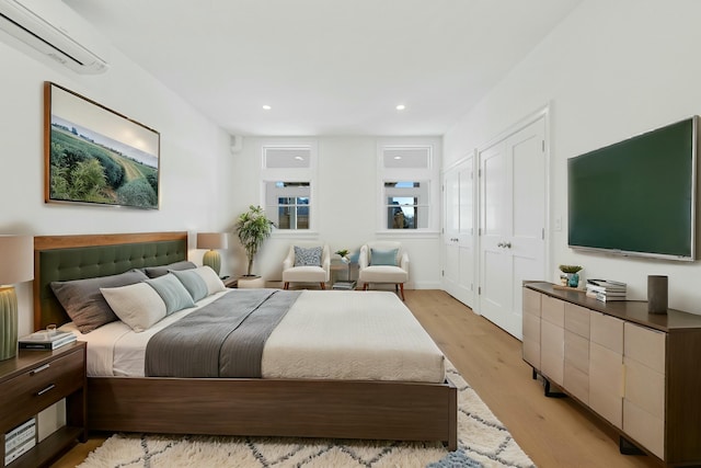 bedroom with a wall mounted AC and light hardwood / wood-style floors