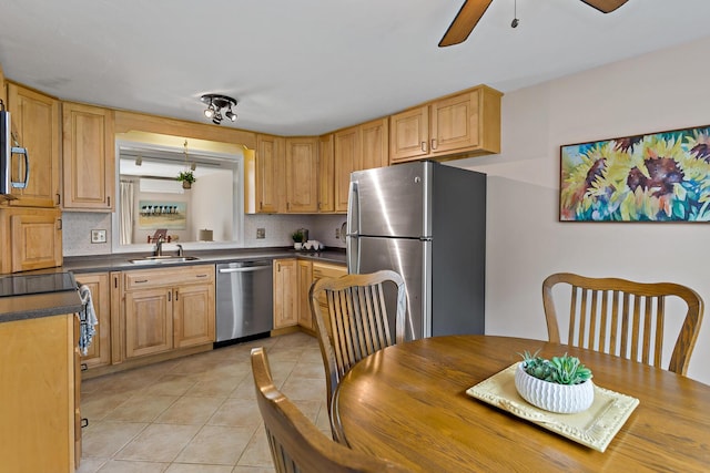 kitchen with a sink, dark countertops, a ceiling fan, appliances with stainless steel finishes, and light tile patterned floors