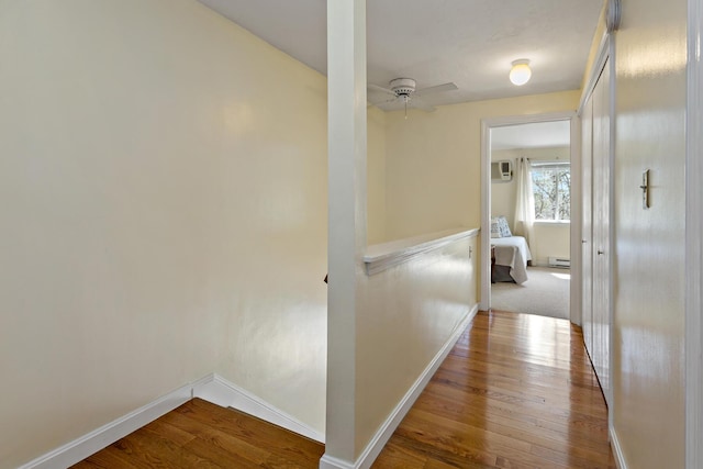 corridor with baseboards, a wall mounted air conditioner, a baseboard heating unit, and wood finished floors
