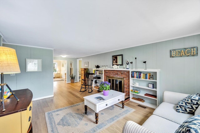 living area with ornamental molding, wood finished floors, and a brick fireplace