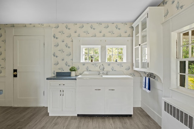 36 Uncle Barneys Rd, West Dennis, MA 02670 - kitchen featuring radiator heating unit, wallpapered walls, light wood-type flooring, healthy amount of natural light, and white cabinetry