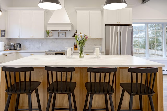 kitchen featuring stainless steel refrigerator, white cabinetry, a kitchen island with sink, a kitchen breakfast bar, and custom exhaust hood