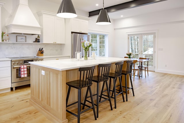 kitchen featuring decorative light fixtures, an island with sink, white cabinets, stainless steel appliances, and custom range hood