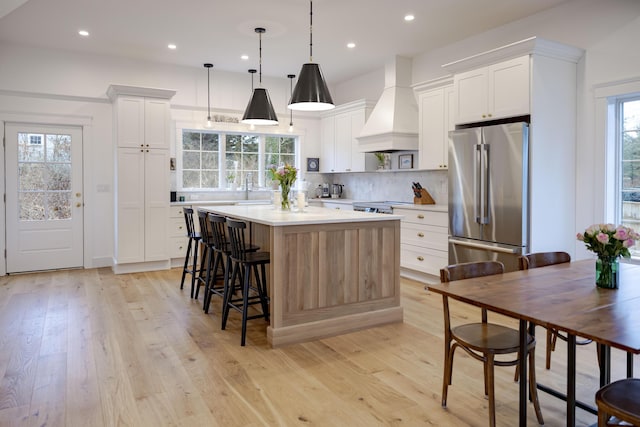 kitchen with stainless steel fridge, custom range hood, white cabinets, a kitchen island, and decorative light fixtures