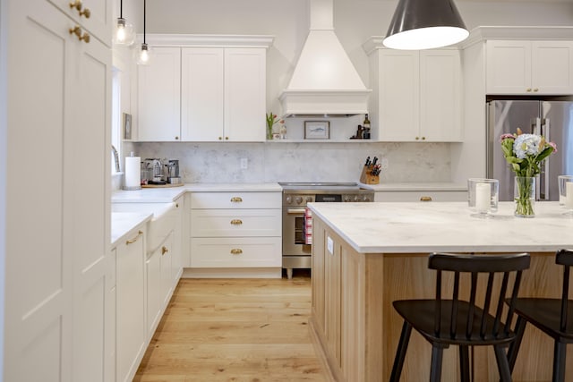 kitchen featuring decorative light fixtures, white cabinetry, custom exhaust hood, stainless steel appliances, and light stone countertops