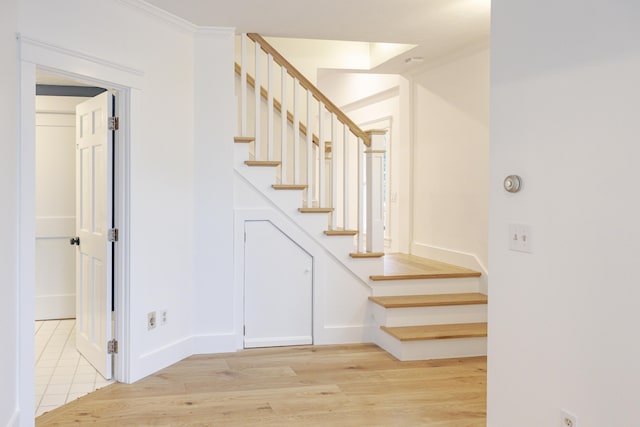 stairway with crown molding and wood-type flooring