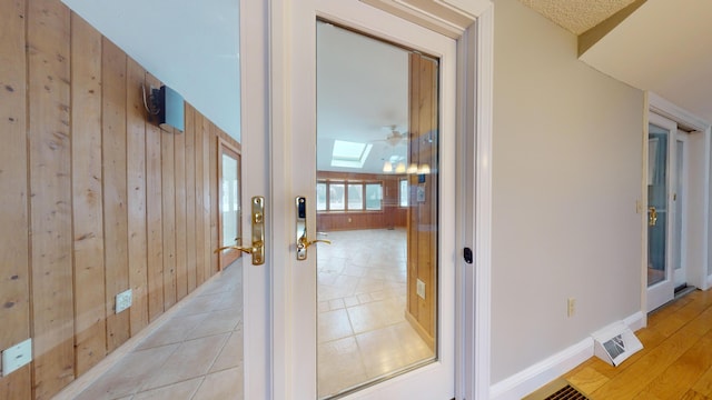 hall with wood walls, light tile patterned floors, and lofted ceiling with skylight