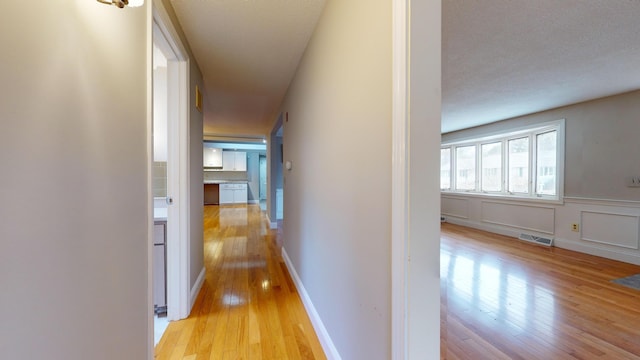 hallway featuring light wood-type flooring and a textured ceiling