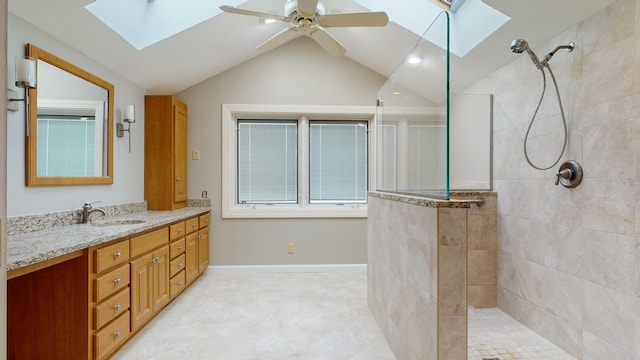 bathroom featuring ceiling fan, vaulted ceiling with skylight, tiled shower, and vanity