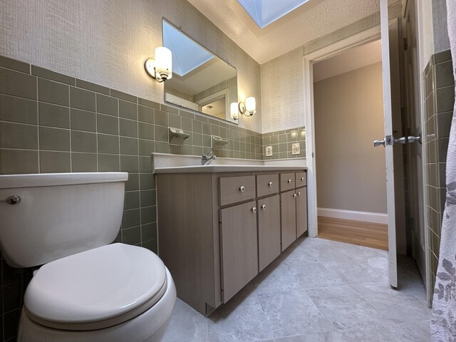 bathroom with tile walls, toilet, vanity, and a skylight