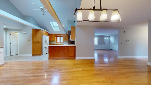 kitchen with decorative light fixtures, white refrigerator with ice dispenser, a skylight, backsplash, and light hardwood / wood-style flooring