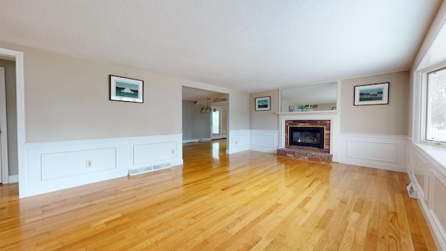 unfurnished living room featuring a brick fireplace, light hardwood / wood-style floors, and a textured ceiling