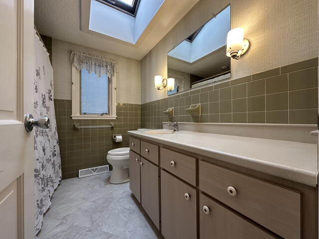 bathroom with vanity, a skylight, tile walls, and toilet