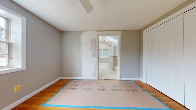 unfurnished bedroom featuring ceiling fan, a textured ceiling, hardwood / wood-style flooring, and a closet