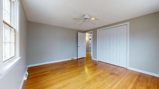 unfurnished bedroom with a closet, ceiling fan, light hardwood / wood-style floors, and a textured ceiling