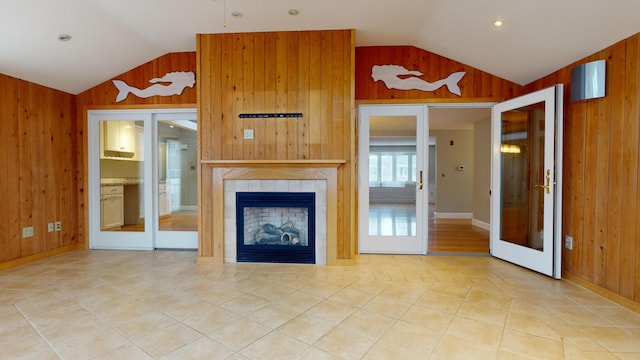 unfurnished living room with tile patterned flooring, vaulted ceiling, french doors, a tiled fireplace, and wooden walls