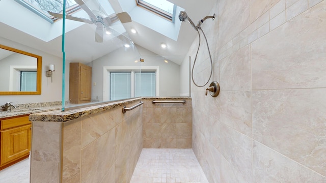 bathroom with ceiling fan, lofted ceiling with skylight, a tile shower, and vanity