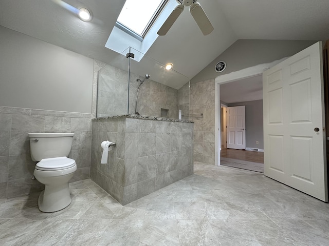 bathroom with toilet, tile walls, a tile shower, lofted ceiling with skylight, and ceiling fan