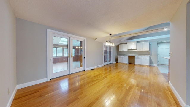 unfurnished living room with light hardwood / wood-style floors, a chandelier, a textured ceiling, and french doors