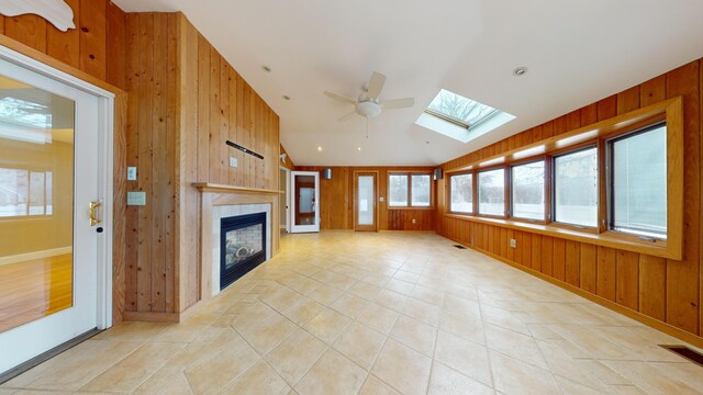 unfurnished living room featuring ceiling fan, wooden walls, a fireplace, and vaulted ceiling with skylight