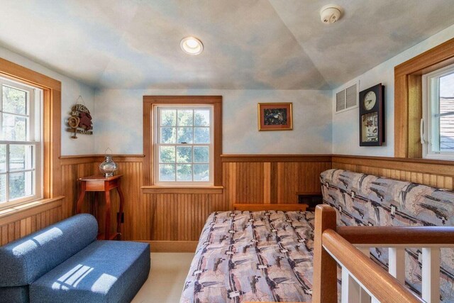 living area featuring a wainscoted wall, visible vents, vaulted ceiling, and a wealth of natural light