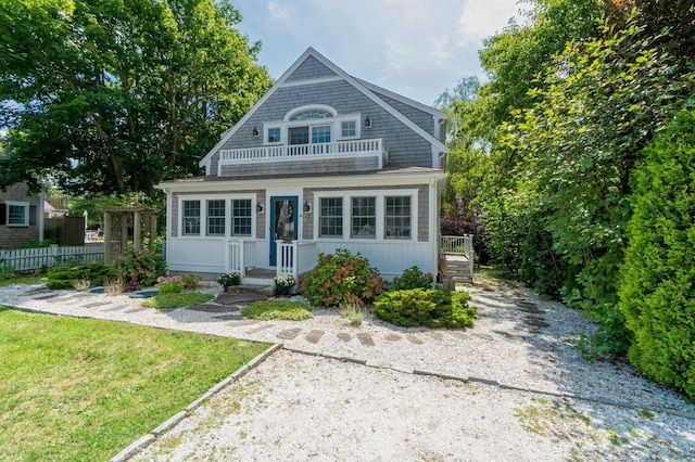 view of front of house with a balcony, fence, and a front yard