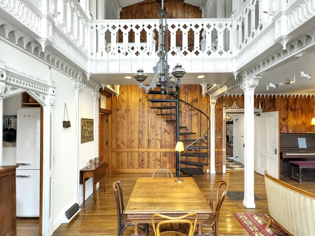 dining area with wooden walls, a high ceiling, hardwood / wood-style floors, and ornate columns