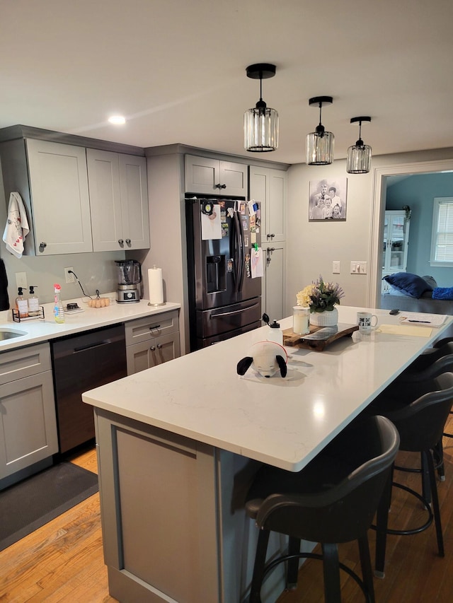 kitchen with dishwashing machine, a breakfast bar area, black fridge with ice dispenser, gray cabinets, and a center island