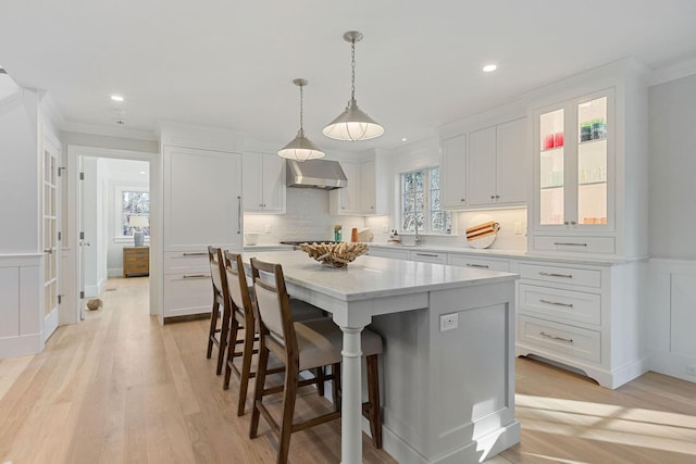 kitchen featuring white cabinetry, plenty of natural light, wall chimney range hood, and a kitchen island