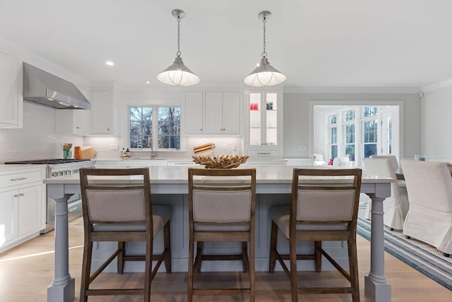 kitchen with white cabinets, a kitchen island, wall chimney exhaust hood, and a kitchen breakfast bar