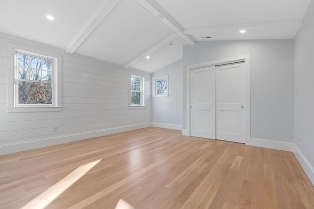 unfurnished bedroom with wood walls, light wood-type flooring, lofted ceiling with beams, and a closet