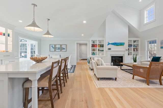 living room with crown molding, built in features, light hardwood / wood-style flooring, and a towering ceiling