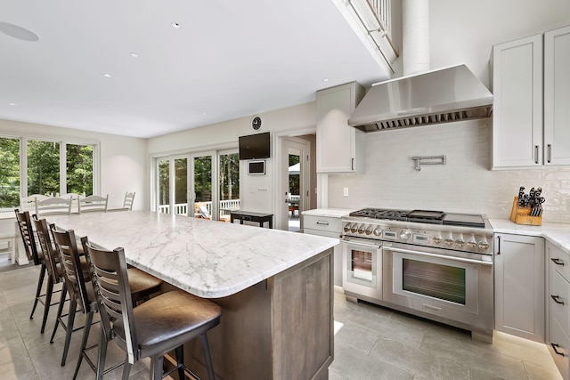 kitchen with a center island, tasteful backsplash, wall chimney range hood, a breakfast bar area, and range with two ovens