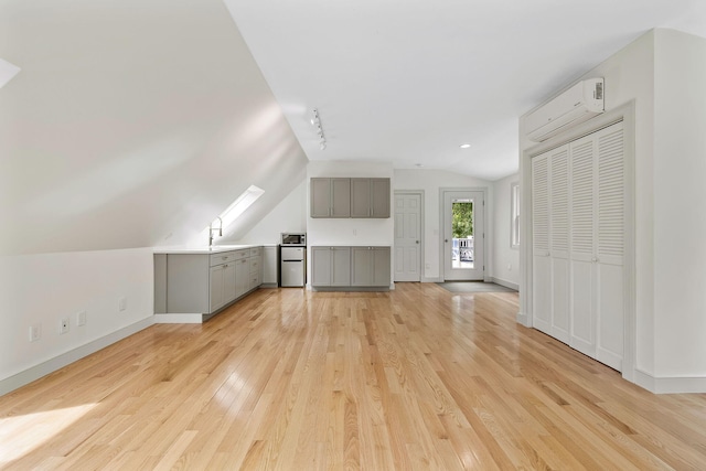 unfurnished living room with an AC wall unit, light wood-type flooring, track lighting, sink, and vaulted ceiling