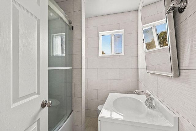 bathroom featuring tile walls, shower / bath combination with glass door, a wealth of natural light, and vanity